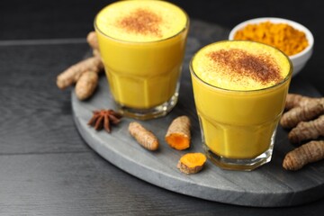 Delicious turmeric latte, powder and rhizomes on black wooden table, closeup
