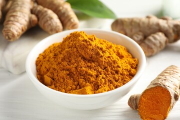 Aromatic turmeric powder and fresh roots on white wooden table, closeup