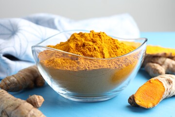 Aromatic turmeric powder in bowl and fresh roots on light blue wooden table, closeup