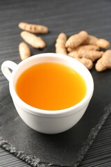 Aromatic turmeric tea and rhizomes on black table, closeup
