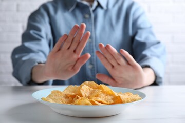 Woman refusing to eat chips at white marble table, selective focus. Food allergy concept