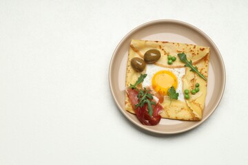 Delicious crepe with egg, bacon, olives and arugula on white table, top view. Space for text