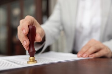 Notary stamping document at wooden table in office, selective focus