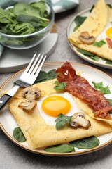Delicious crepes with eggs, bacon and mushrooms served on grey table, closeup. Breton galette