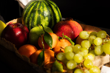 Close up of freshly harvested fruits on a rustic wooden tray with dark background illuminated by the morning sun coming through the window. Dark food of fruits