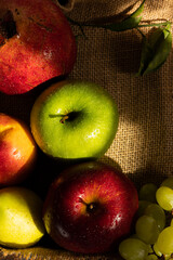 Vertical image of fresh fruits. Apples, pomegranate, pear, peach and a bunch of green grapes on rustic cloth on a wooden tray with copy space