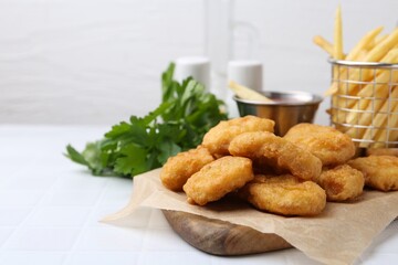 Tasty chicken nuggets, potato fries and sauce on white tiled table, closeup. Space for text