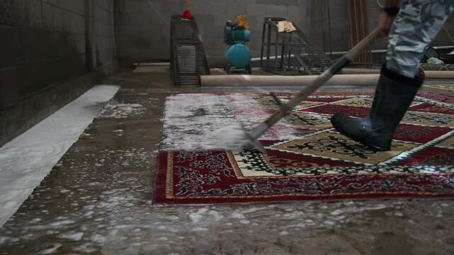 A specialist in camouflage pants and rubber boots uses a squeegee to remove residual foam and cleaning solution, marking the final stage of deep cleaning in a professional laundry.