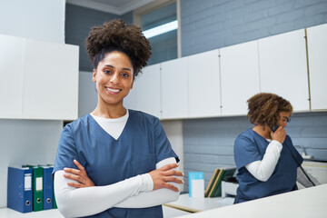 Confident Smiling Nurse in a Medical Reception While Colleague Manages Phone Calls