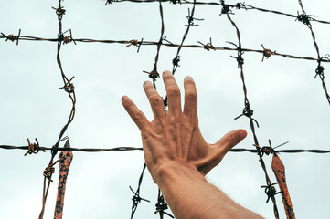 men's hand behind a barbed wire fence against the sky.