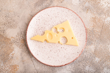 Piece of cheese with holes on ceramic plate on brown concrete, top view, copy space