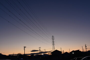 夕暮れ時の山の向こうに見える送電線と鉄塔
