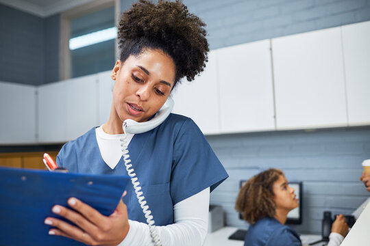 Female Healthcare Worker Taking Notes While Using a Phone in a Modern Medical Office