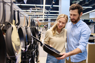 A couple is happily shopping for various cookware items together in a modern retail store