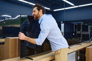 A man joyfully embraces a TV in an electronics store displaying modern gadgets and design