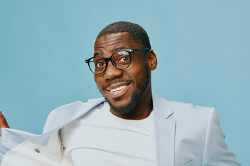 Portrait of a cheerful young man in stylish light suit against a soft blue background, smiling...