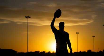 Silhouetted rugby player holding the ball, determined mood, against a sunset backdrop
