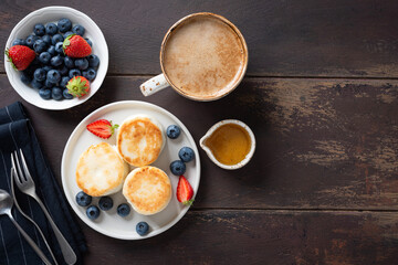 Curd cheese fritters Syrniki with berries, honey and cup of coffee on a wooden table background, top view with copy space