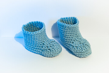Pair of light blue colored and crocheted baby socks against a white background