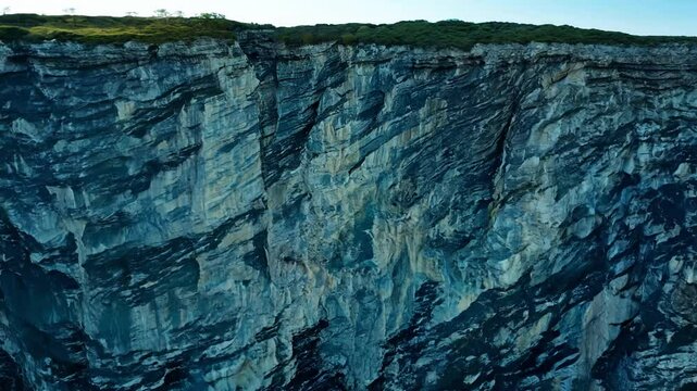 Zoom out video of a rocky cliff face with distinct horizontal layers, emphasized by the angled side sunlight, establishing geological strata
