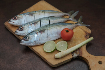 Some Fresh Mackerel Fish with slice of lemon, red tomato and lemon grass On Wooden Chopping Board,...
