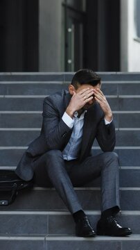 Vertical Format Video of Upset businessman in frustration outside office department. Fired unhappy caucasian bearded man losing job crying and sitting on stairs. Unemployment. Crisis