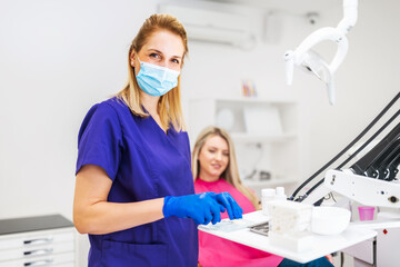 Dentist is repairing teeth of young woman. She is preparing dental filling.