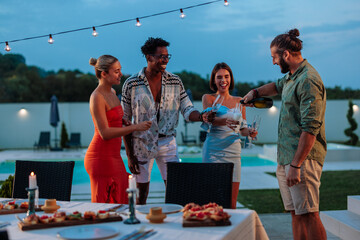 Friends pouring sparkling wine at a luxury poolside dinner party