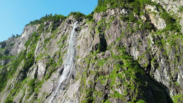 Waterfall flowing over rocky and sunny mountain terrain