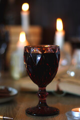Books, lit candles, red wine, snacks and various deocration on the table. Dark academia or Halloween concept. Selective focus.