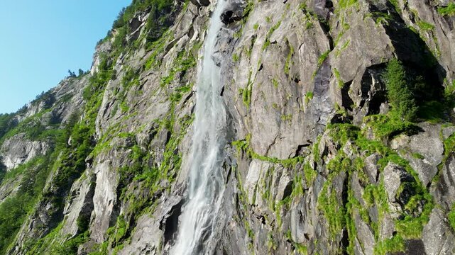 Waterfall flowing over rocky and sunny mountain terrain