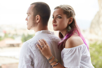 Obraz premium woman with colorful hair and a bright top leans gently against a man wearing a light shirt. They share a peaceful moment while admiring stunning scenery in the background