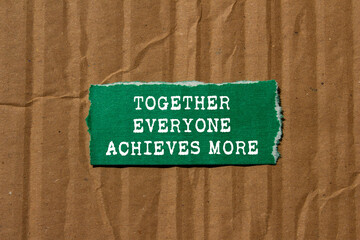 Together everyone achieves more message written on ripped torn green paper piece on cardboard background. Conceptual together everyone achieves more symbol. Copy space.