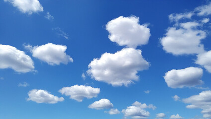 Fototapeta premium Fluffy white clouds floating in a bright blue sky, perfect for serene backgrounds, wallpapers, and calming design projects.