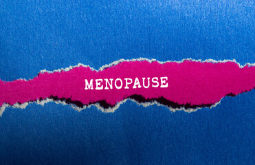Menopause message written on ripped torn blue paper on pink background. Conceptual menopause symbol. Copy space.