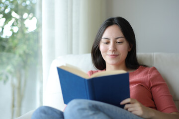 Fototapeta premium Satisfied asian woman reading a paper book at home