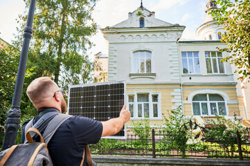 Man holding photovoltaic solar panel in front of historical building. Concept of integration of...