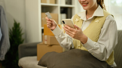A Close-up image of a woman happily completing an online purchase using her phone and credit card...