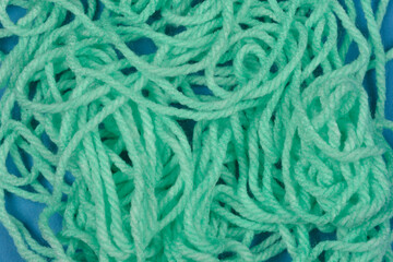 A close-up, top-down view of a tangled pile of light green yarn against a solid blue background, showcasing its texture and disarray