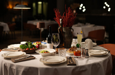 Close-up of a round table set with plates, cutlery, glasses, napkins, and a decorative centerpiece in a dimly lit restaurant