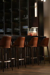 A row of bar stools lined up against a sleek bar counter with illuminated shelves displaying glassware and bottles