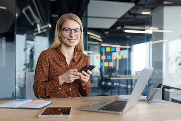 Portrait of a successful woman inside the office, businesswoman with phone in hands smiling and...