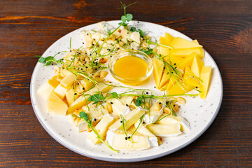 Cheese platter with honey and garnishes on wooden table