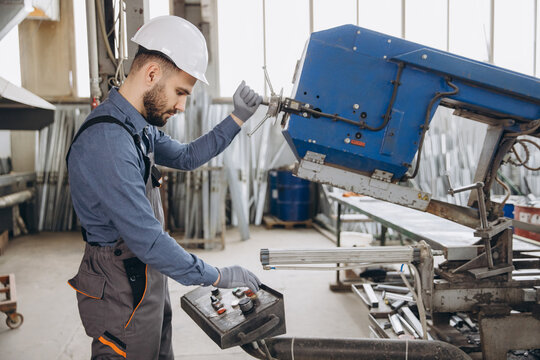 Factory male worker operating industrial band saw for aluminum and pvc windows and doors production