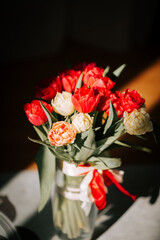 Vase holding vibrant tulips reflecting sunlight near a mirror in a spring setting