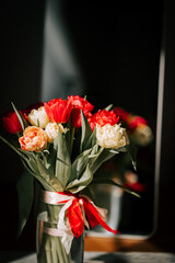 Bright tulips in a vase reflect in a sunlit mirror enhancing the spring atmosphere in a cozy space