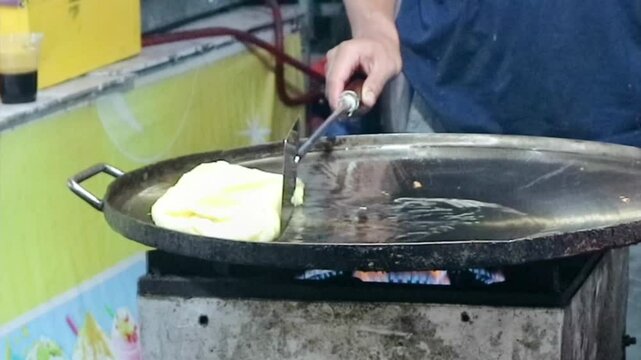 A vendor prepares an martabak telur or egg, an Indonesian specialty. Fried in hot oil on a flat pan.And use a spatula to cook .Focus on food.blurred,shake video,exposure,nighty noise