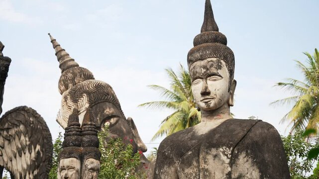 Big stone Statues of Buddha among palm trees in park in Laos
