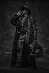Black and white portrait of brutal man, sheriff in cowboy hat, long leather coat, vest over shirt,...