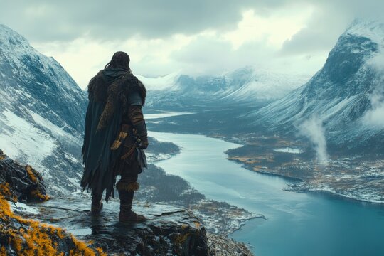 Person stands on a cliff overlooking a fjord surrounded by snow-capped mountains in a dramatic landscape - Powered by Adobe